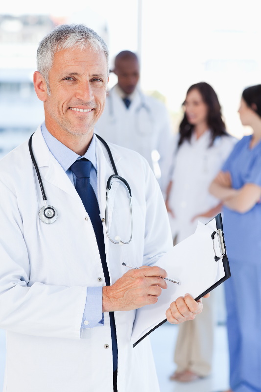 mature doctor smiling in foreground & other medical staff in backround